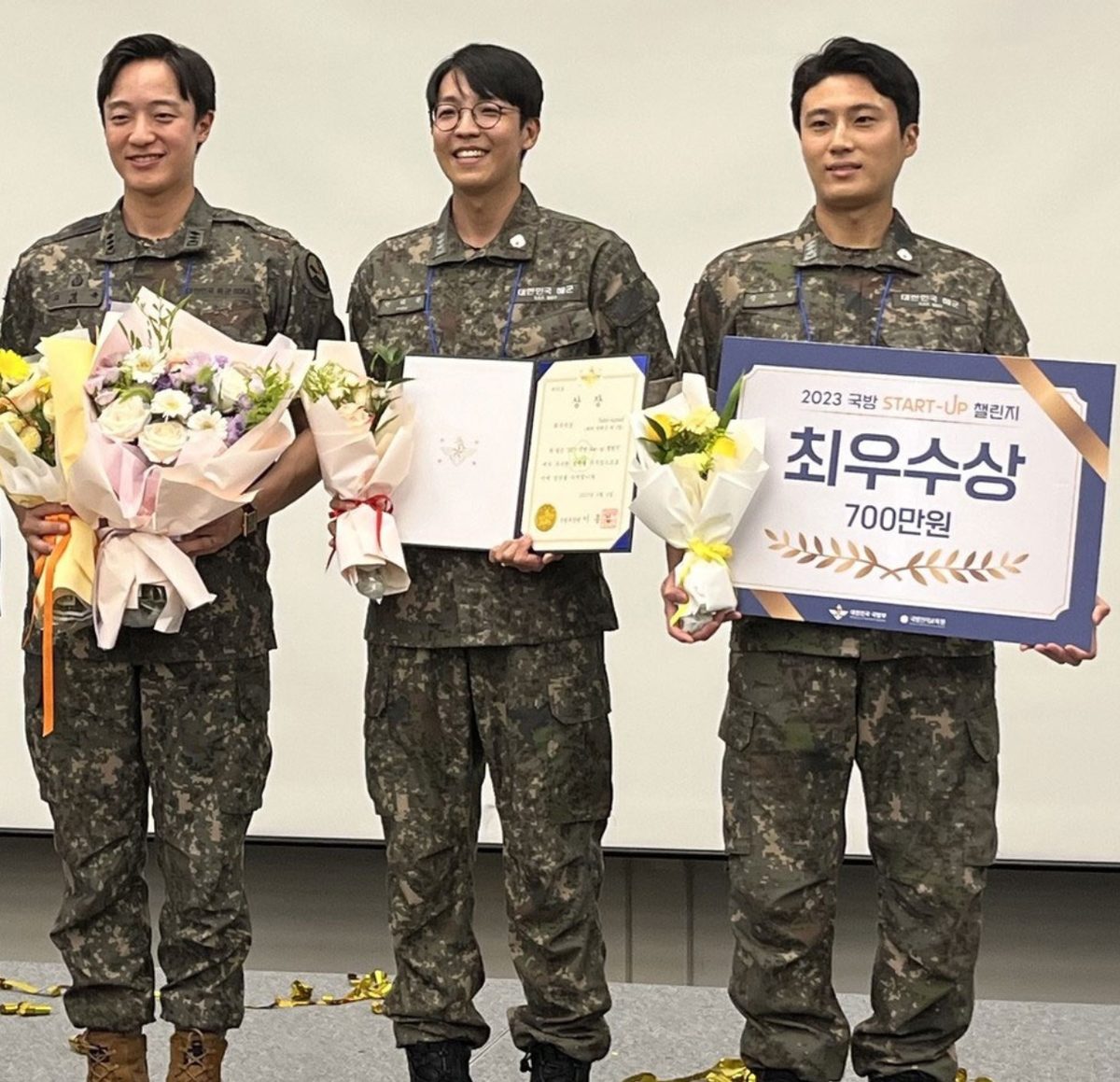 Three of Sanidoc's founding doctors in South Korean military uniform, holding flowers, a certificate and an award board at the 2023 Defense Start-up Challenge